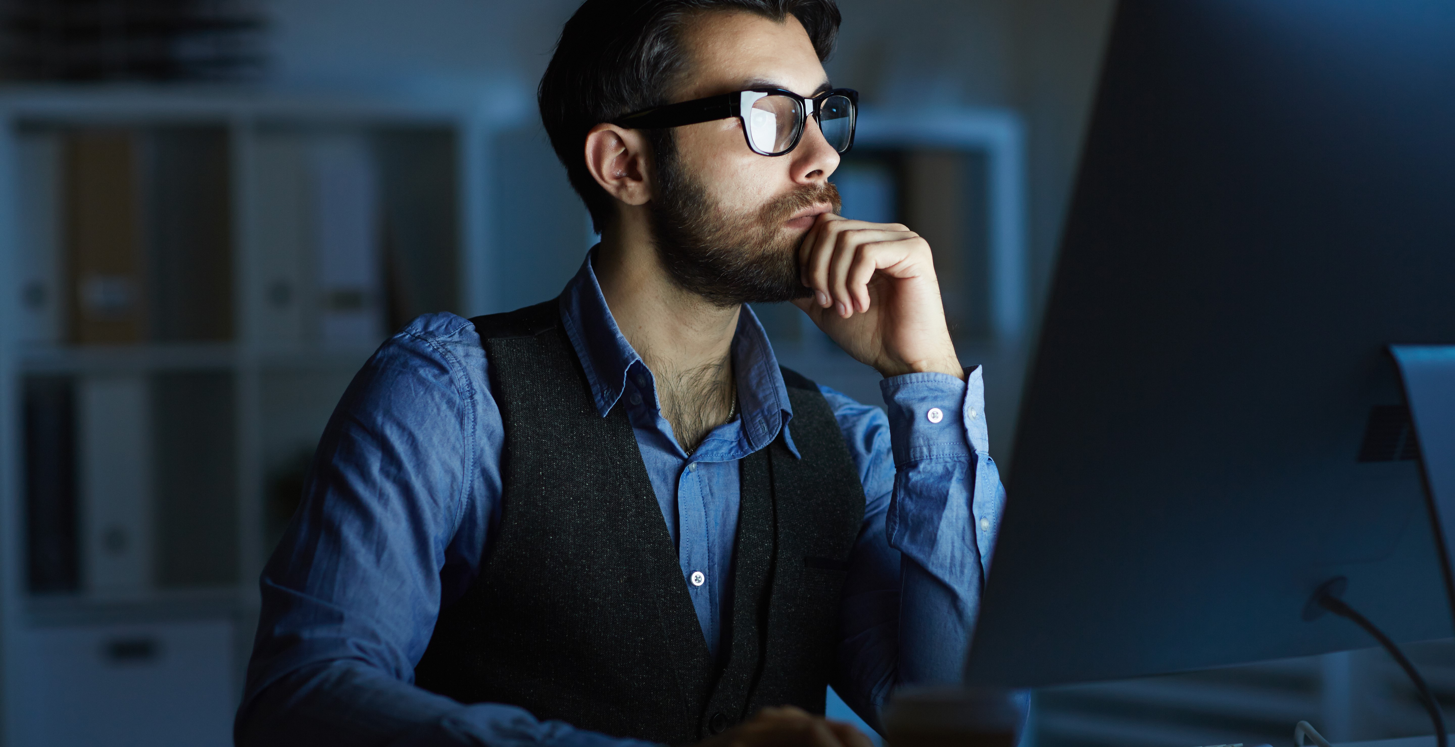 Bespectacled man working at a desktop computer.
