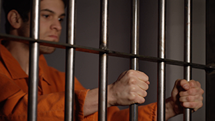 Prisoner in orange jumpsuit holding cell bars